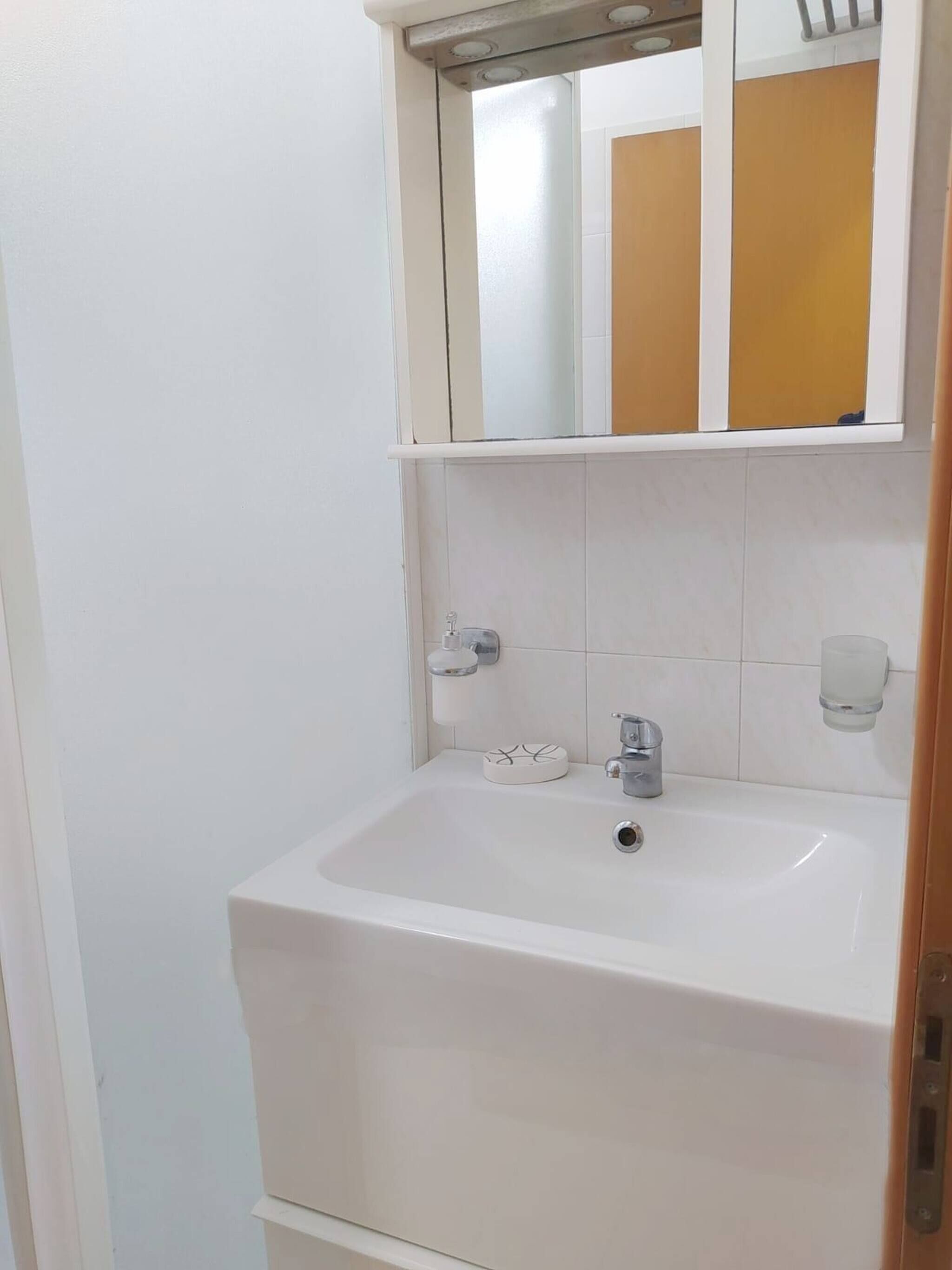 Un baño con un lavamanos blanco, un espejo y un perchero para toallas.
