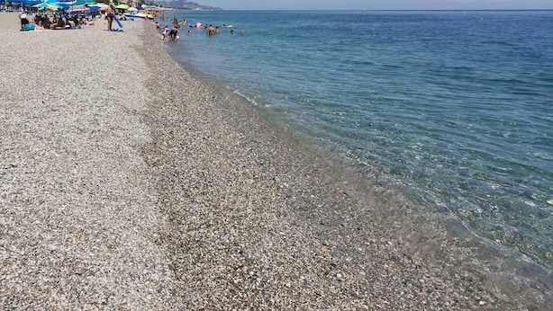 A pebble beach with clear water, umbrellas, and people. - Blue Garden Home - Fondachello (Mascali)