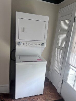 A compact washer and dryer unit in a corner with a door and window nearby.