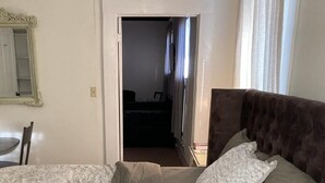 A bedroom with a bed, a chair, a mirror, and a door leading to another room. - Joy Apartment #3 centrally located.  (Anniston)