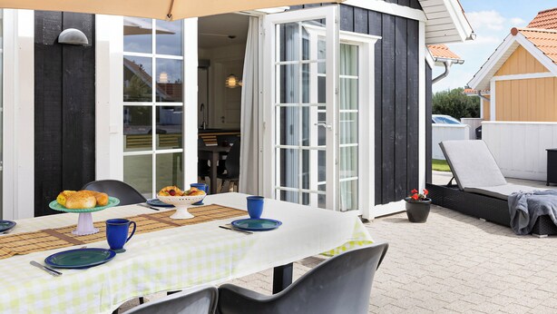 An outdoor dining area with a table set for two, a wicker lounge chair, and a potted plant. - Cozy, central house near the sea (Brenderup)