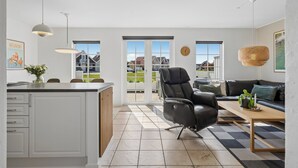 A spacious living area with a black leather sofa, a wooden coffee table, and a view through large sliding glass doors to the outside. - Cozy, central house near the sea (Brenderup)