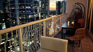 Ein Balkon mit Blick auf hohe Gebäude, einem Tisch mit Stühlen und einem Hängekorbsessel.