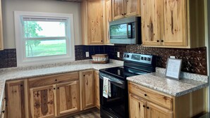 A kitchen with wooden cabinets, a Bosch microwave, a stove, and a window with a view of greenery.