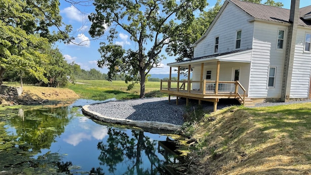 Ein Haus mit einer Holzterrasse und einem Teich im Garten.