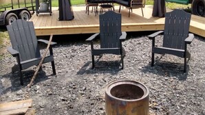 A covered outdoor seating area with a grill, a fire pit, and a green bus in the background.