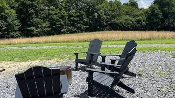 Two Adirondack chairs on a gravel surface with a grassy field and trees in the background.
