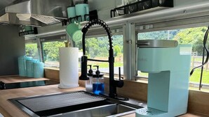 A kitchen with a stainless steel sink, a coffee machine, and a window with a view of greenery.