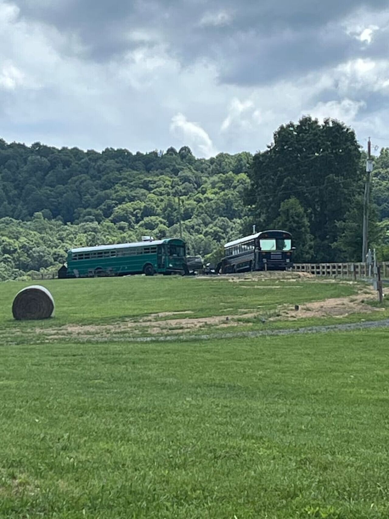 A green bus parked in a grassy field with a hay bale in the foreground.