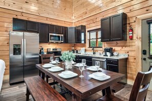 A wooden cabin interior with a kitchen, dining table set for four, and a refrigerator.