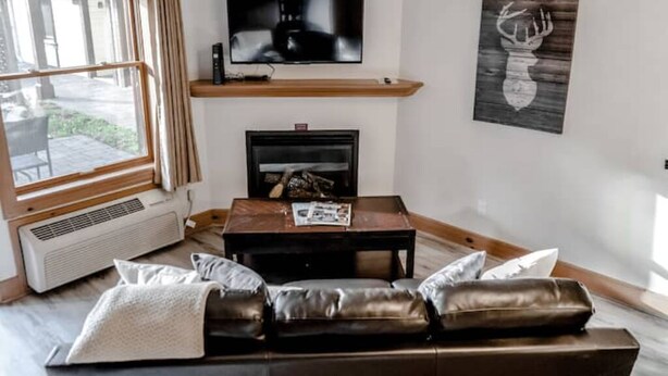 Ein Wohnzimmer mit Ledersofa, Kamin, Wandfernseher und einem fenster mit Vorhängen.