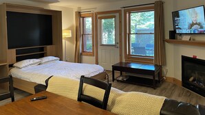 Ein Hotelzimmer mit Bett, Fernseher, Kamin, Esstisch und zwei Fenstern.