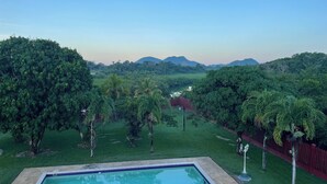Ein rechteckiger Pool mit schimmerndem Beckenrand, umgeben von einer Rasenfläche mit Palmen und einem roten Zaun.