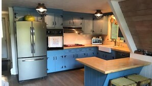 A modern kitchen with blue cabinets, stainless steel appliances, and a wooden island. - Direct Waterfront, Year-Round, A-Frame Cabin (Antrim)