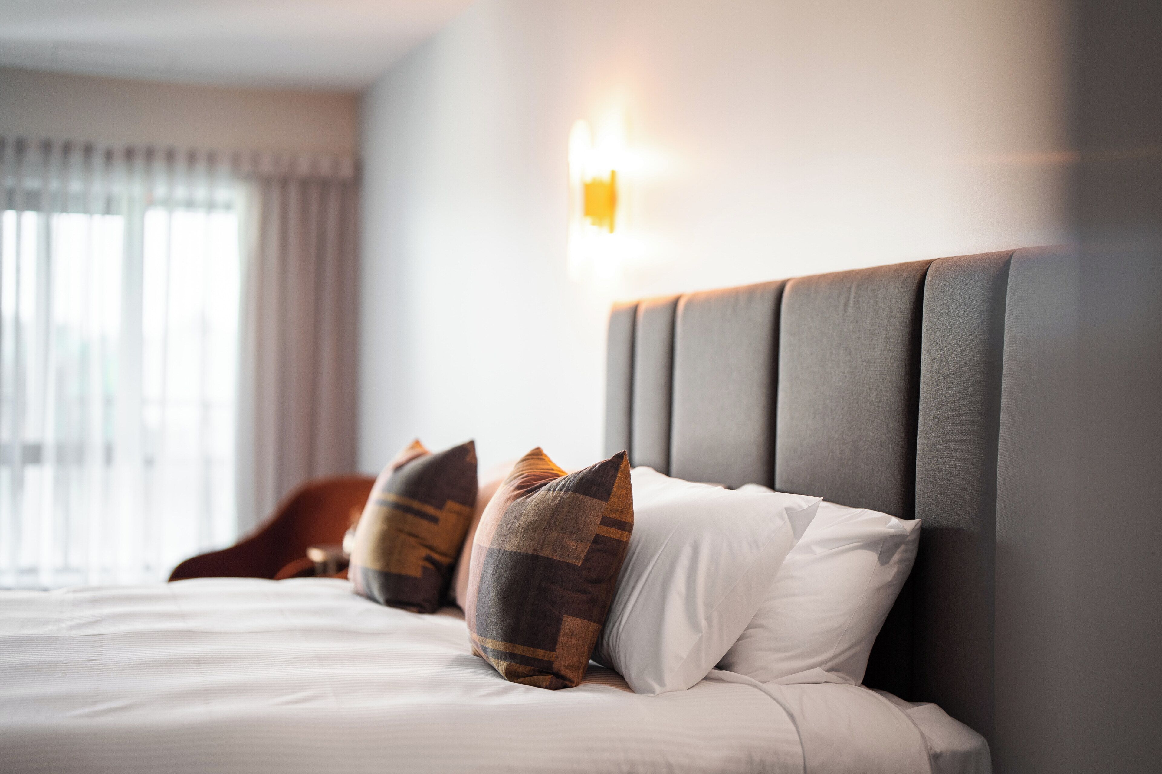 Una cama bien hecha, con un cabecero gris, ropa de cama blanca y almohadas estampadas.