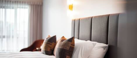 Una cama bien hecha, con un cabecero gris, ropa de cama blanca y almohadas estampadas.