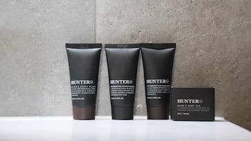 Three Hunter hand and body wash bottles and a bar soap on a white surface against a textured wall.
