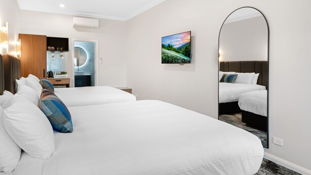 Habitación de hotel con dos camas, un espejo grande, un cuadro y un baño moderno con un espejo circular.