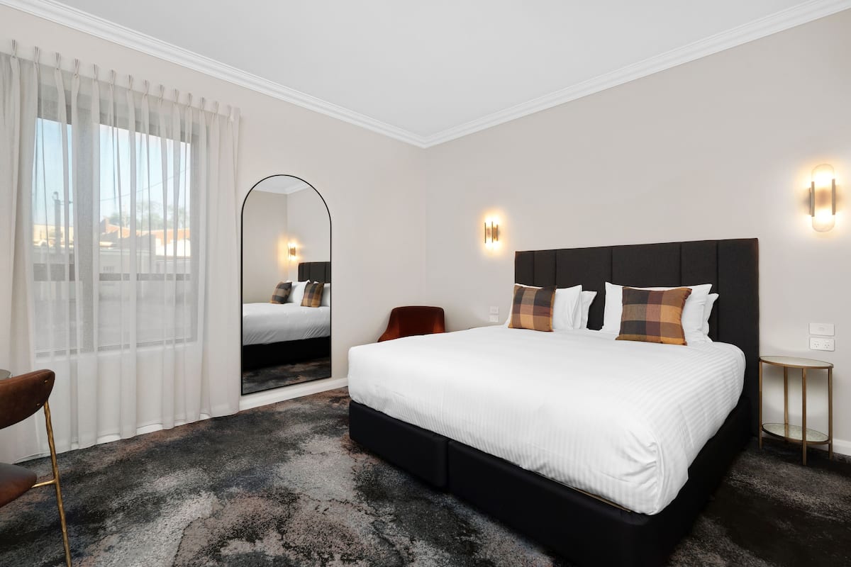 A modern hotel room with a large bed, a mirror, and two wall-mounted lights.