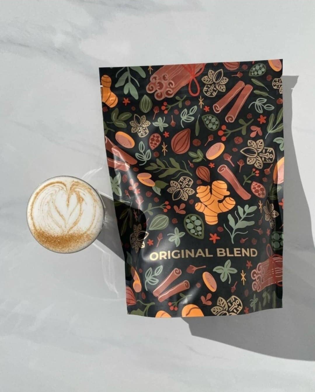 A coffee cup with latte art and a bag labeled "ORIGINAL BLEND" on a marble surface.
