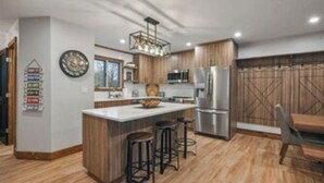 A modern kitchen with wooden cabinets, a central island with stools, stainless steel appliances, and a decorative clock on the wall. - Ski Side Getaway < 1 Mile From Mountain  (Tannersville)