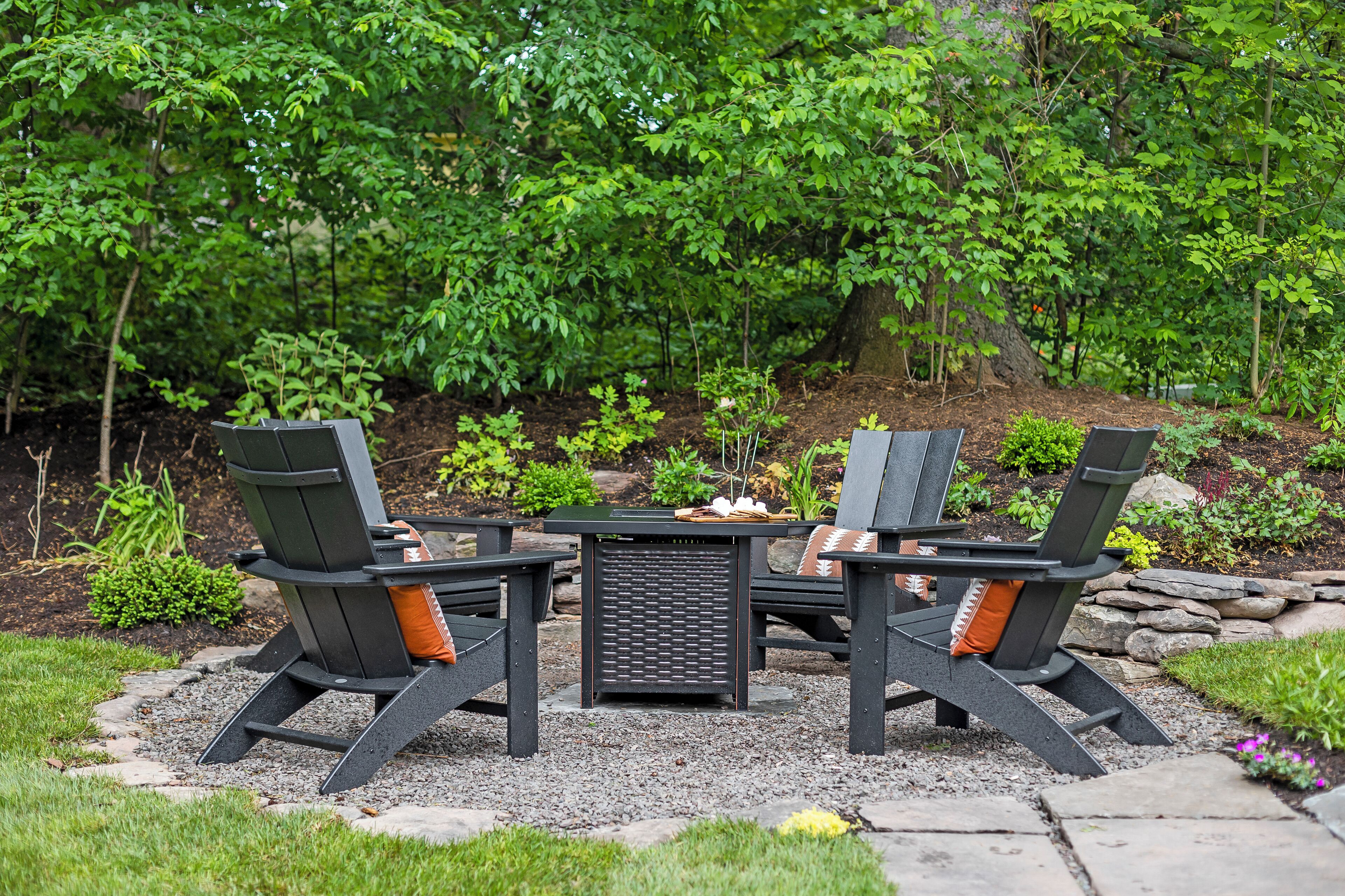 Une terrasse avec une table et quatre chaises Adirondack, entourée d’un jardin où poussent différentes plantes et bordée d’un sentier en pierre.