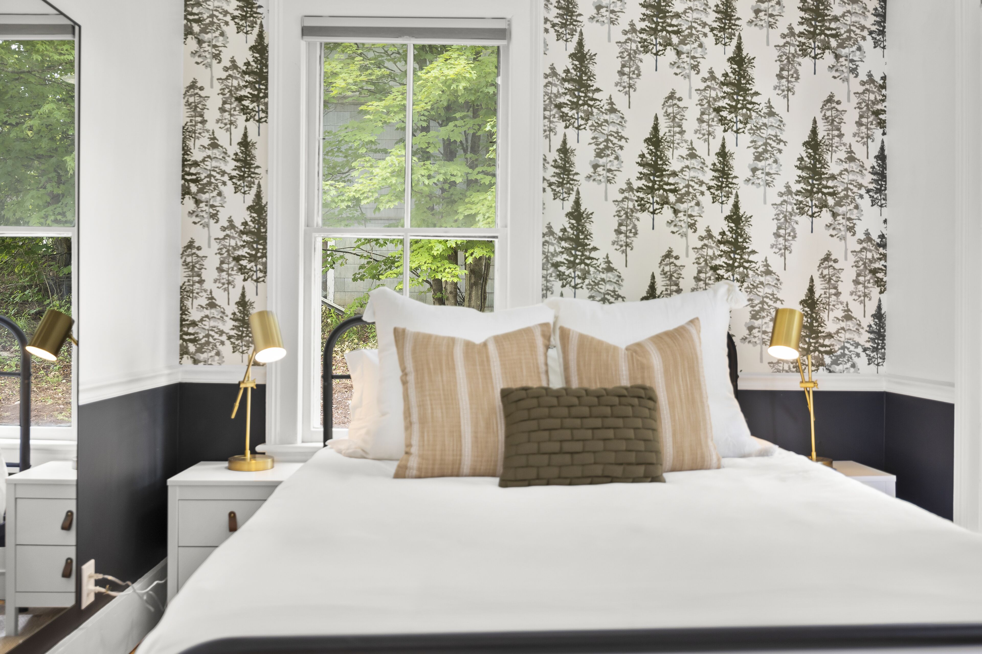 A bedroom with a large bed, two bedside tables, and a window with a view of trees.