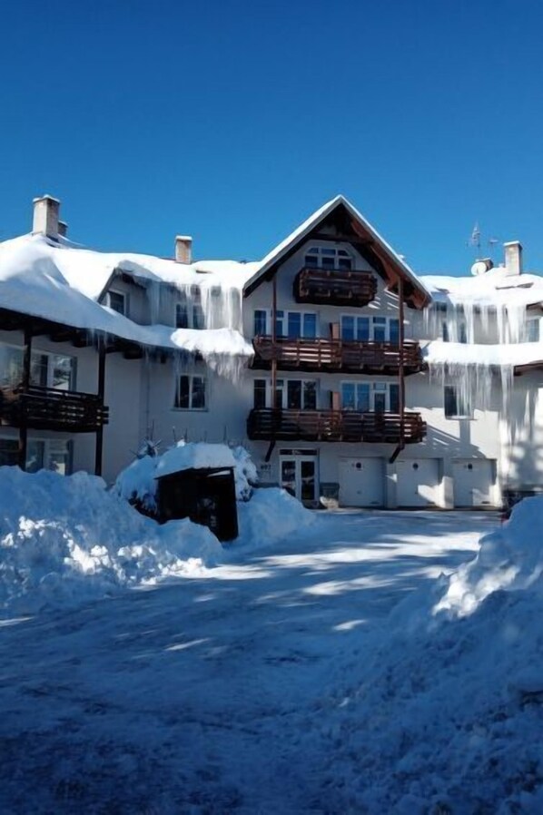 Un edificio de varios pisos con tejado nevado y balcones, rodeado de nieve.