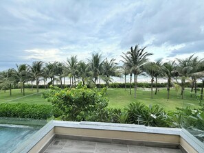 A poolside view with a grassy area, palm trees, and a beach in the background. - VILLA PHONGLIEM (Cam Lam)