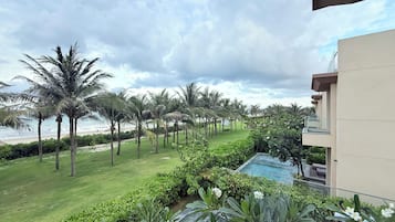 A lush garden with palm trees and a pool, overlooking a beach.