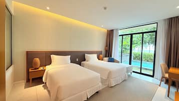 A hotel room with two beds, a large window with a view of greenery, a small table, and a chair.