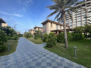 A pathway leading to a modern building with a palm tree and well-maintained greenery. - VILLA PHONGLIEM (Cam Lam)