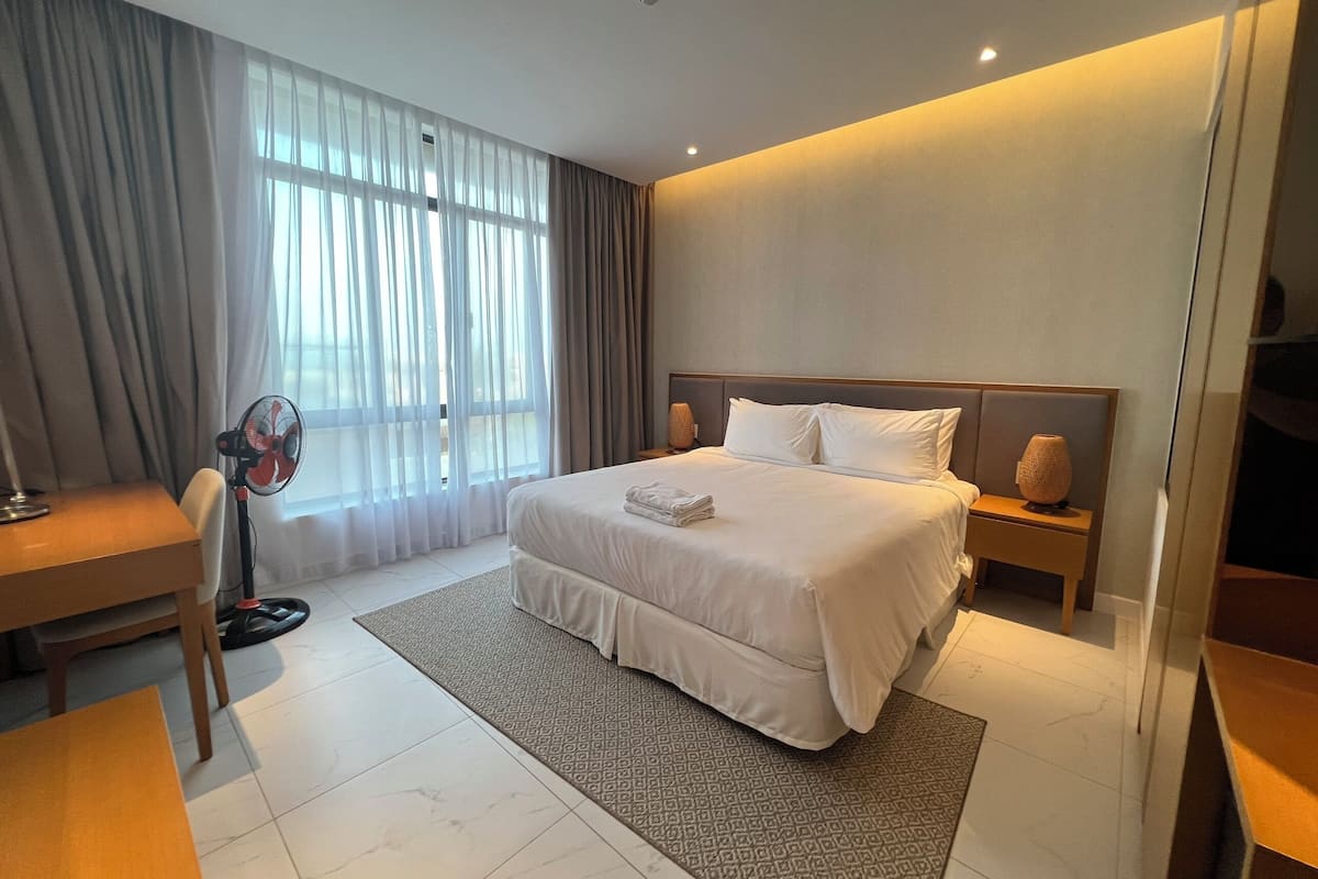 A modern hotel room with a large bed, a desk, and a standing fan.