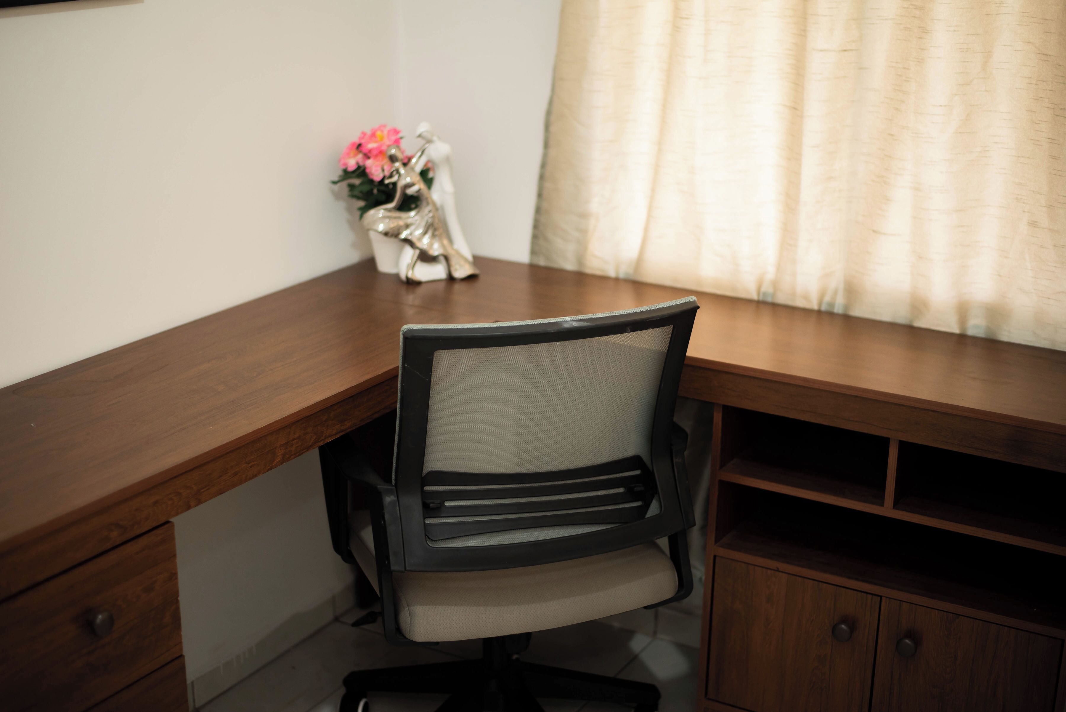 Un escritorio de madera con una silla, una pequeña estatua y un florero con flores.