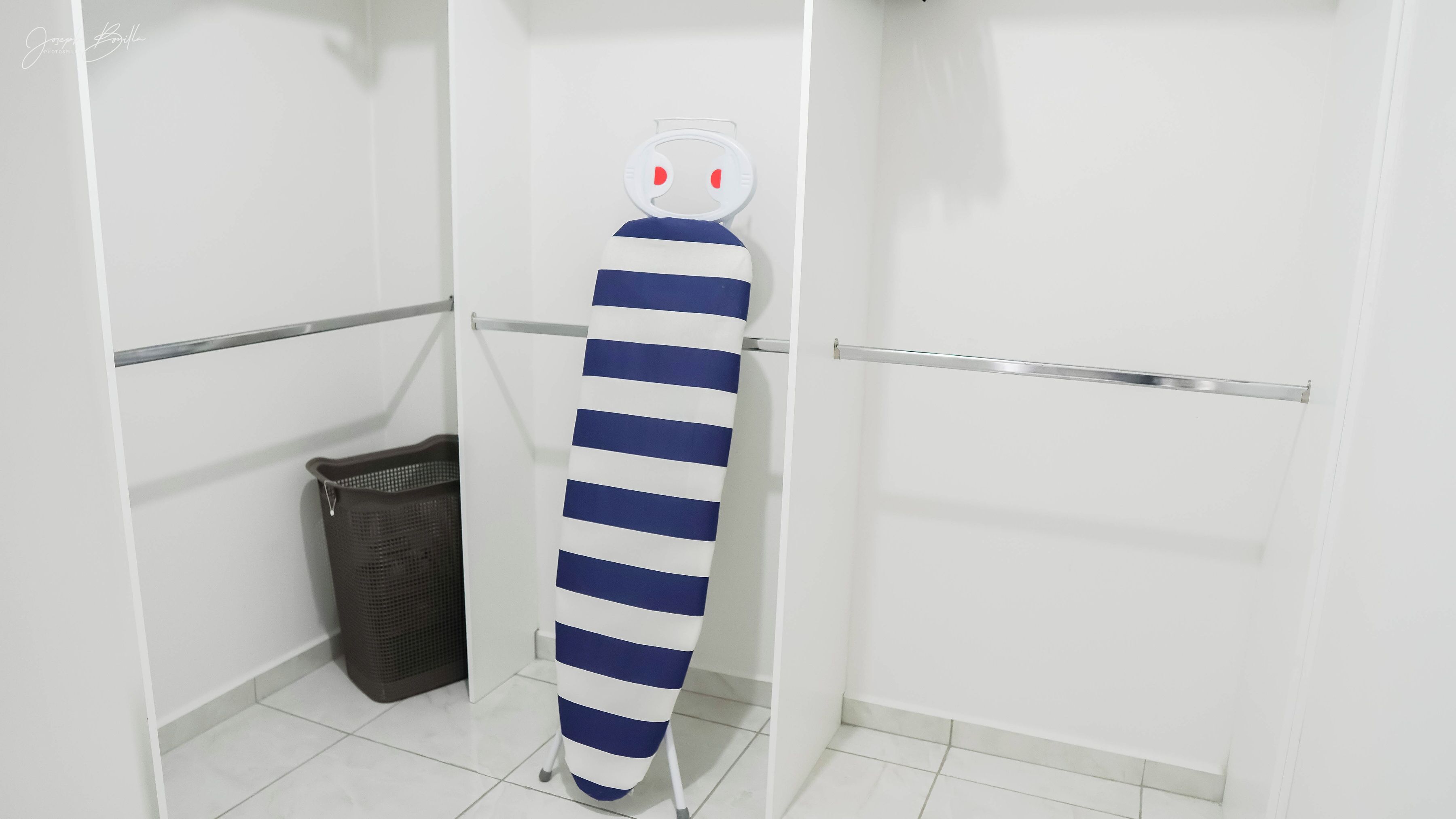 Une salle de bain aux murs blancs, une serviette rayée suspendue à un porte-serviettes, une poubelle et une porte.