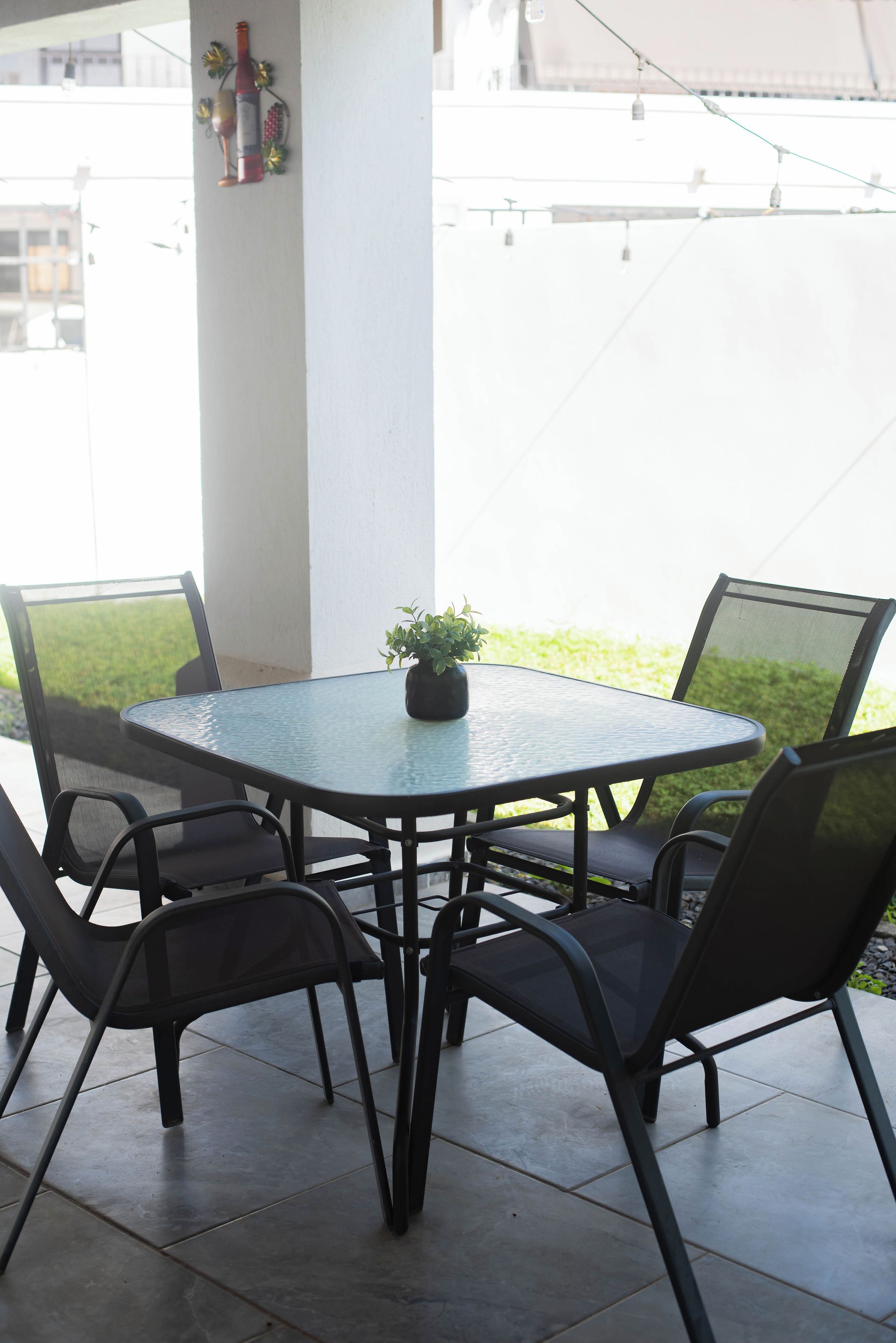 A round table with four chairs, a potted plant, and a decorative bottle on the wall.