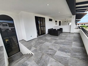 A modern outdoor patio area with a stone floor, black furniture, and a glass door entrance. - House in San Miguel, Res. San Andres (San Miguel)