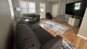 Un salon comprenant un canapé d’angle, un téléviseur à écran plat, un petit meuble et une porte décorée d’une guirlande.