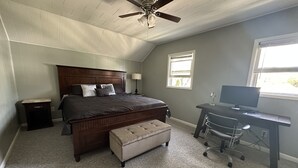 Une chambre à coucher avec un grand lit, un bureau, une chaise, un ventilateur de plafond et une fenêtre.