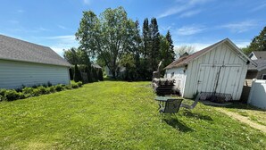 Un jardin bien entretenu avec une pelouse, une petite table et des chaises, et un abri de jardin.