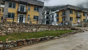 A multi-story building with balconies, a stone retaining wall, and a grassy area in front.