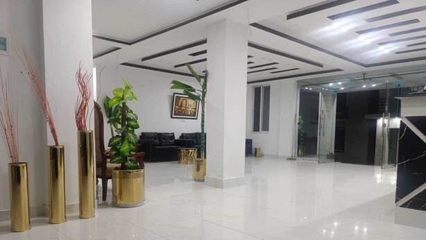A modern lobby with a polished floor, a reception desk, and several potted plants.