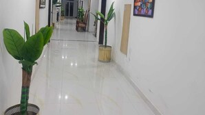 A clean, well-lit hallway with a polished floor, potted plants, framed artwork, and a door at the end.