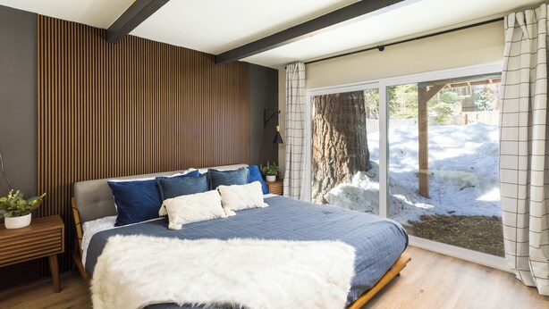 Een moderne slaapkamer met een groot bed, een wand van houten panelen en uitzicht op een besneeuwd landschap.