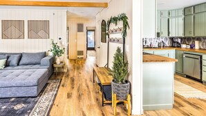 Een moderne woonkamer met een grijze bank, houten vloeren en een centraal gelegen eiland met een plant in pot.