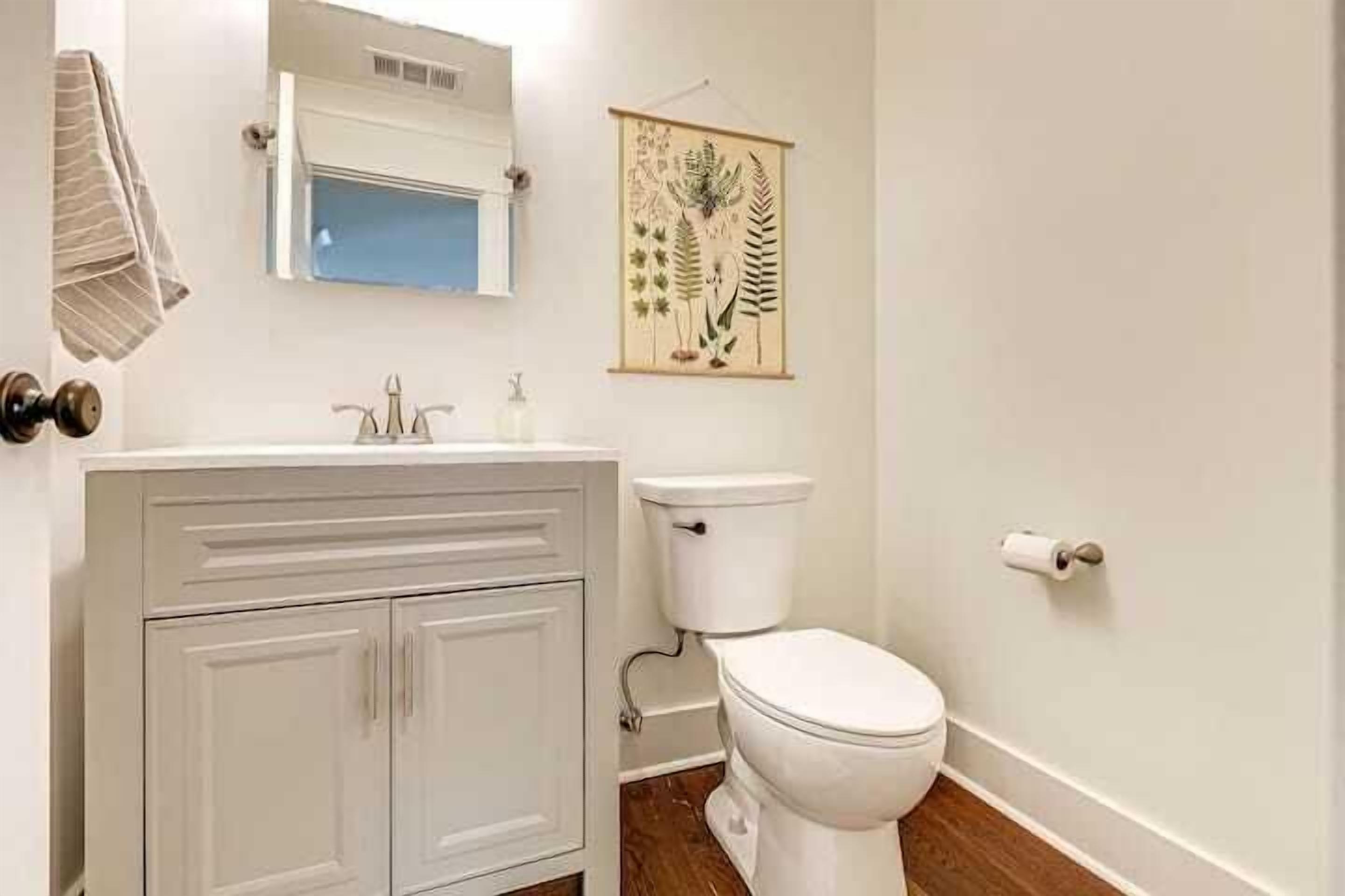 Une salle de bain avec un lavabo blanc, des toilettes et une estampe botanique encadrée au mur.