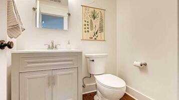 Un baño con un lavamanos blanco, un inodoro e impresión enmarcadas de motivos botánicos en la pared.