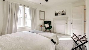 Une chambre avec deux lits, un ventilateur de plafond, un fauteuil vert et une cheminée.