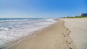 Een strand met een heldere lucht, golven en gebouwen op de achtergrond.
