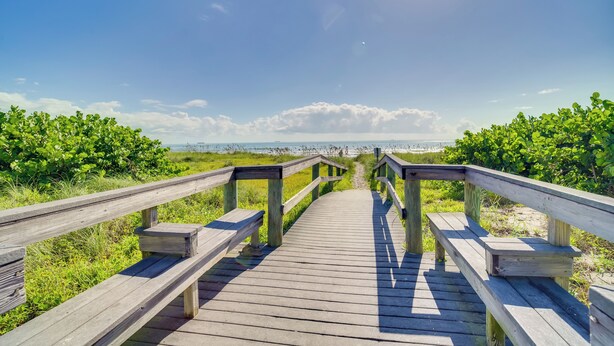 Een houten looppad naar een strand, met een heldere lucht en verre horizon.